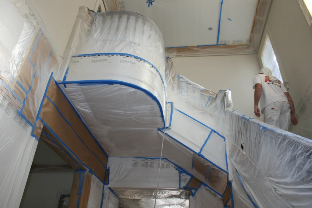 Prep work in a house covered in plastic and taped in preparation for interior trim painting.