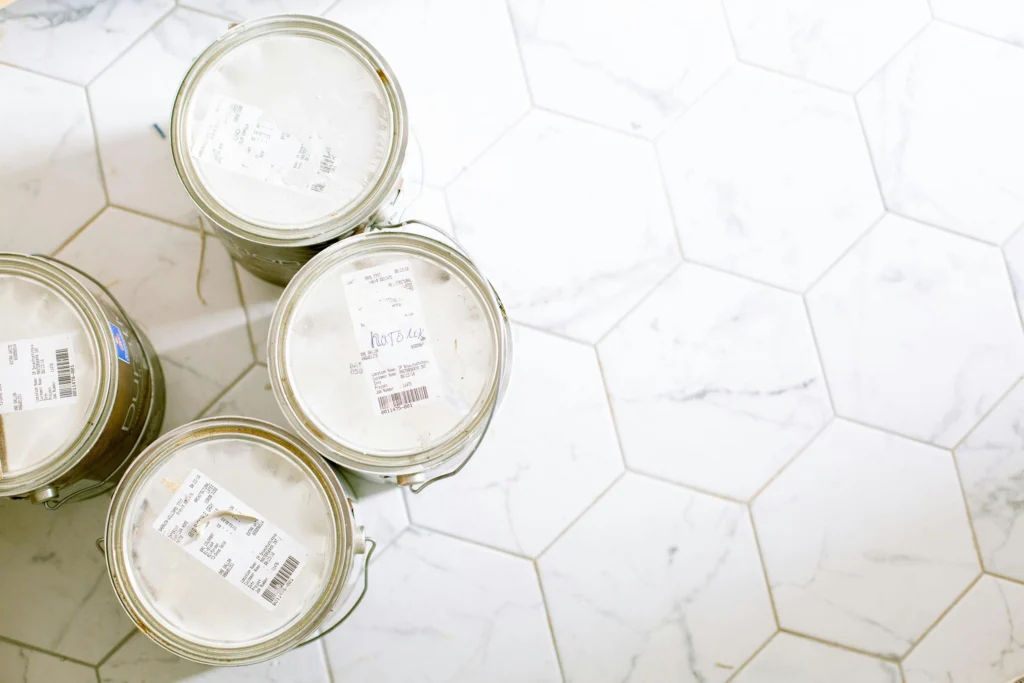 A variety of different types of paint in cans to choose from on a white tile floor.