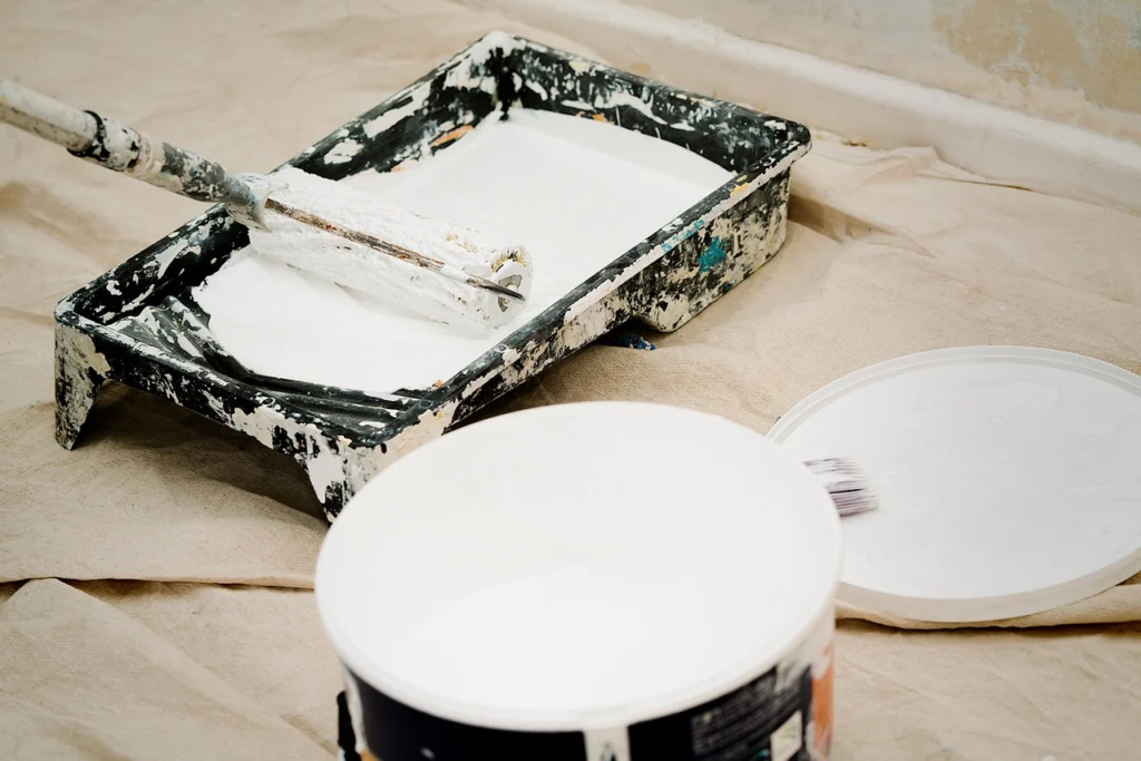 Paint can and roller in paint tray of white paint prepping for interior painting.