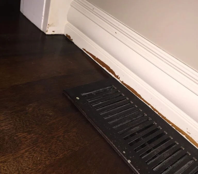 White trim baseboards with paint scratched off near floor and corners that needs to be resanded and repainted.