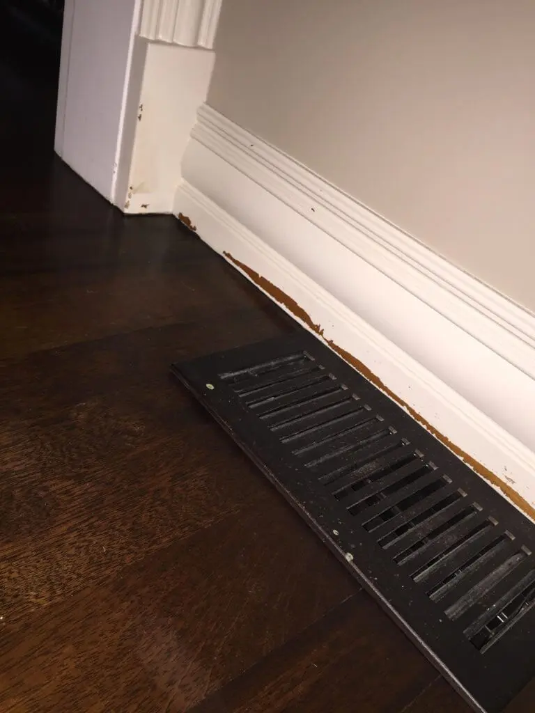 White trim baseboards with paint scratched off near floor and corners that needs to be resanded and repainted.