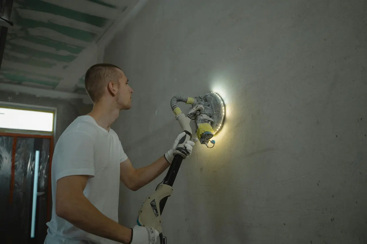 A person sanding an interior wall inside.