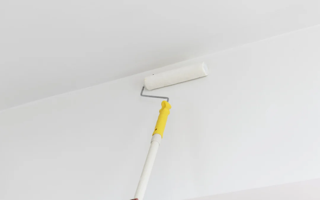 Person using a paint roller to paint the ceiling and the wall.
