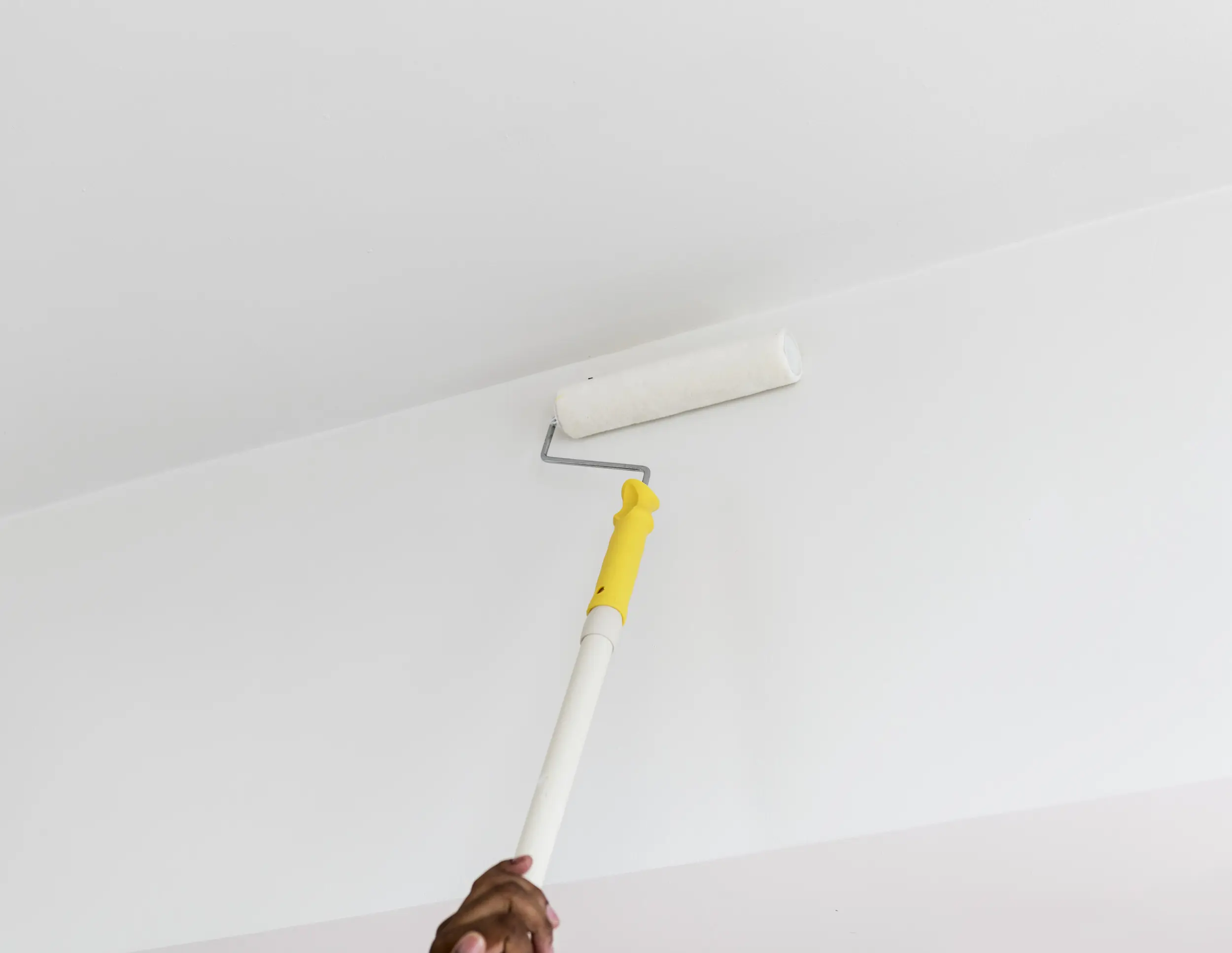 Person using a paint roller to paint the ceiling and the wall.