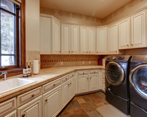 A perspective view of a kitchen in all white with dark wood countertops and flowery wallpaper.