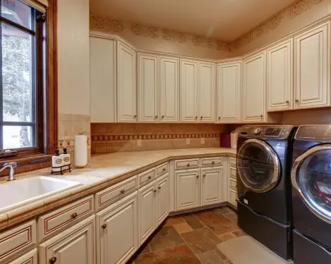 A perspective view of a kitchen in all white with dark wood countertops and flowery wallpaper.