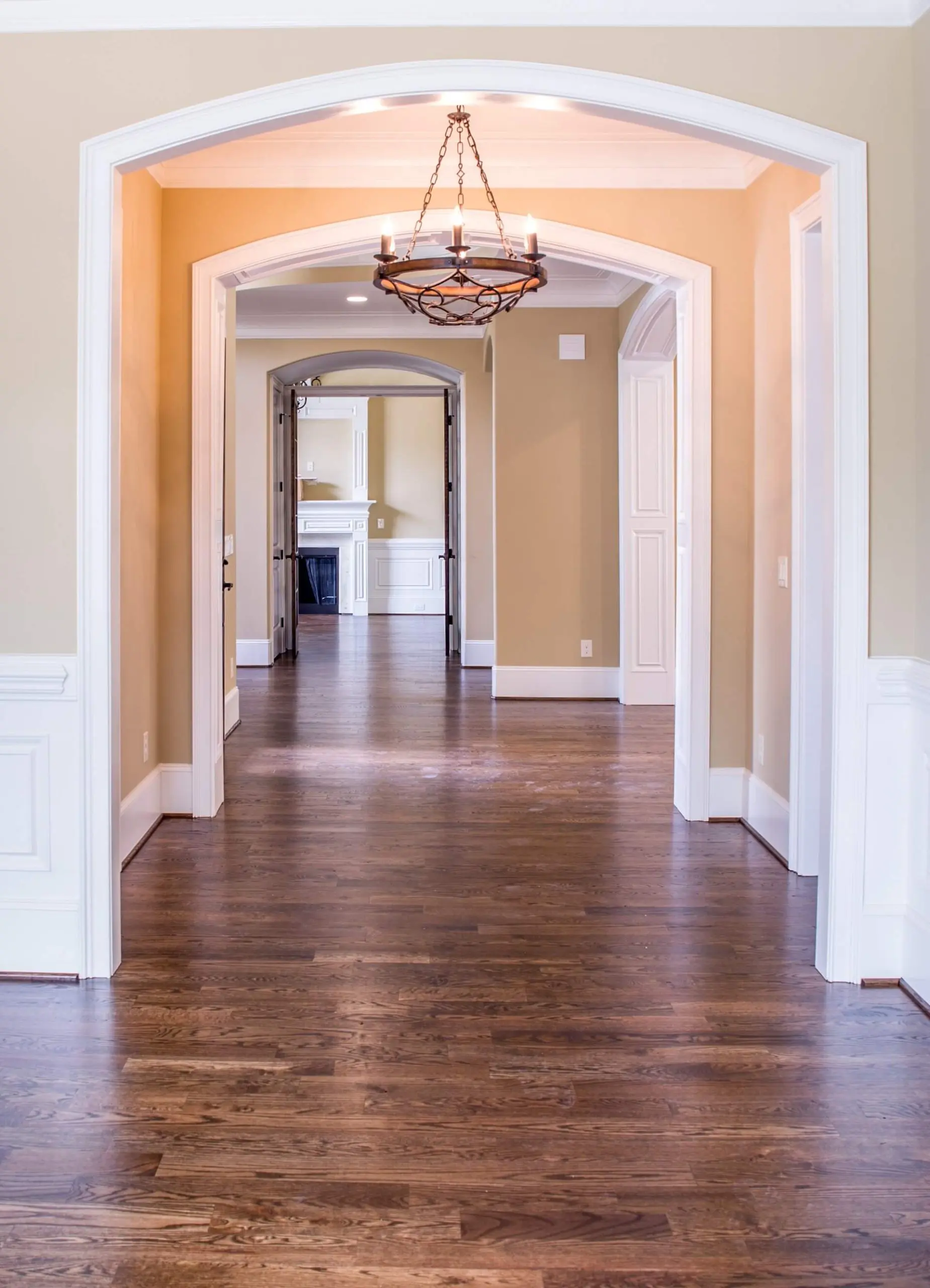 A long hallway with arched entrances, hardwood floors, and walls painted by Imhoff in a creamy beige tone.