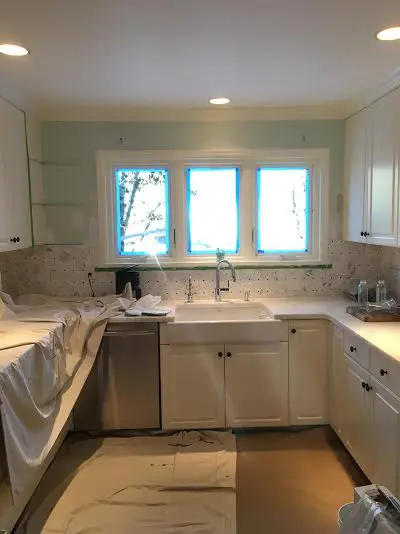 A kitchen in white and stainless steel with enameled cabinets and two chandeliers hanging above the island.
