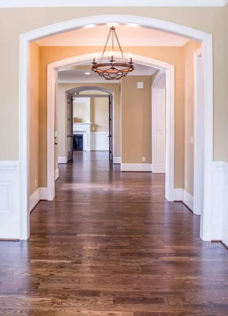 A long hallway with arched entrances, hardwood floors, and walls painted by Imhoff in a creamy beige tone.