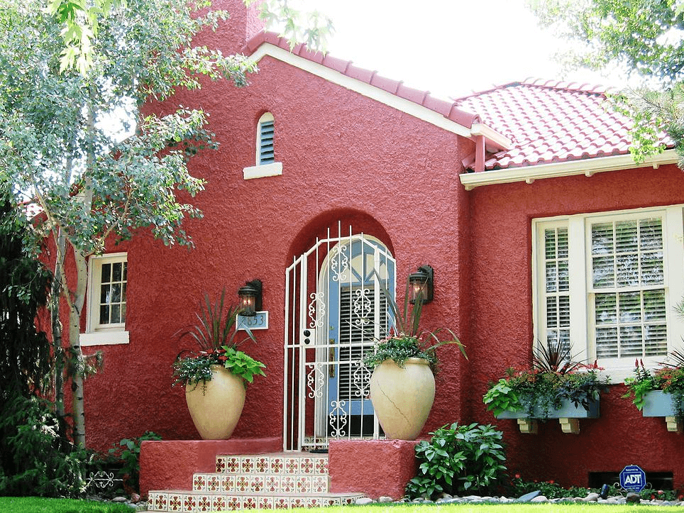 The front of a home with a red brick or stone exterior, gated door, and lovely garden view.