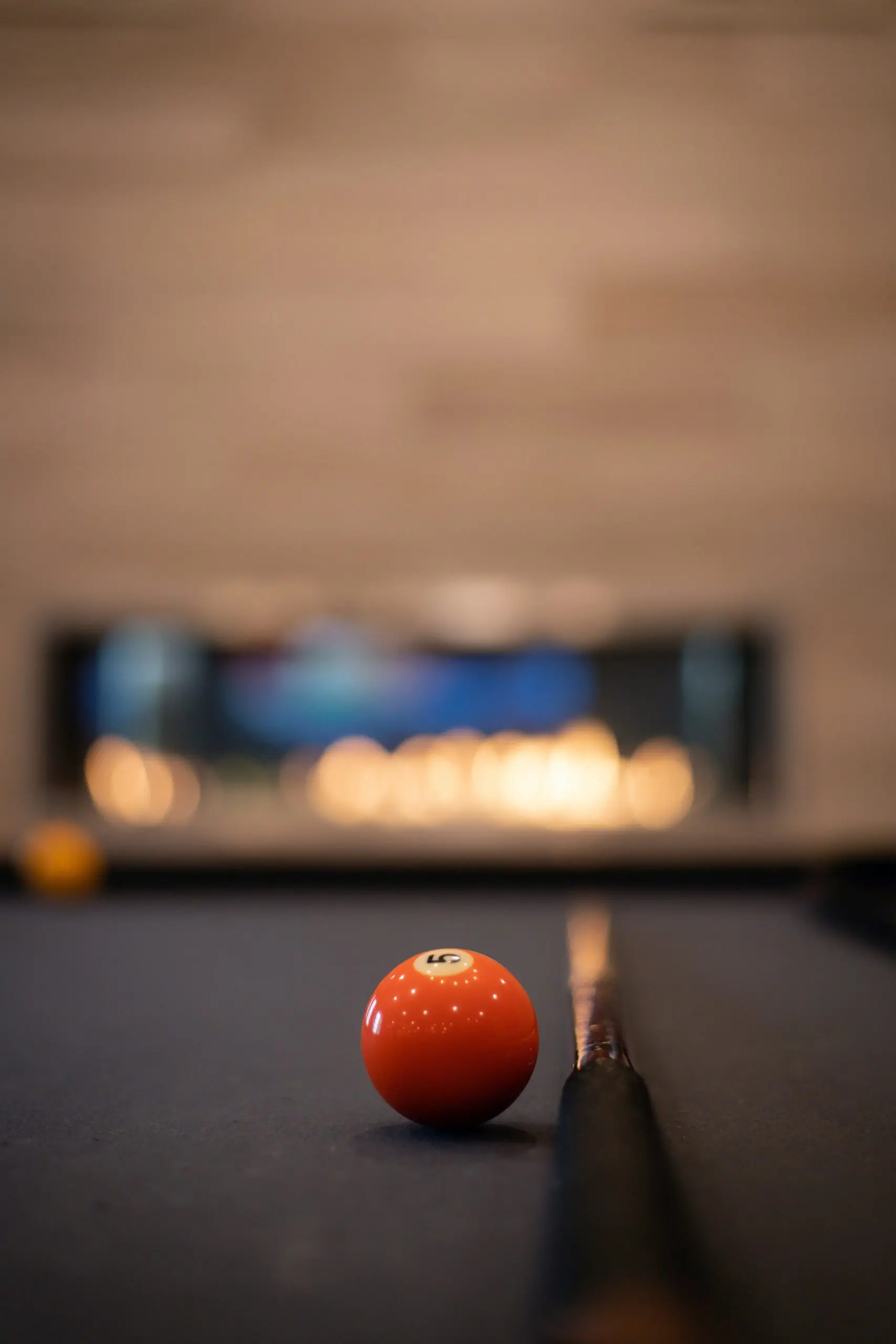 A pool table with a pool cue stick and the orange number 5 ball against a blurred background.