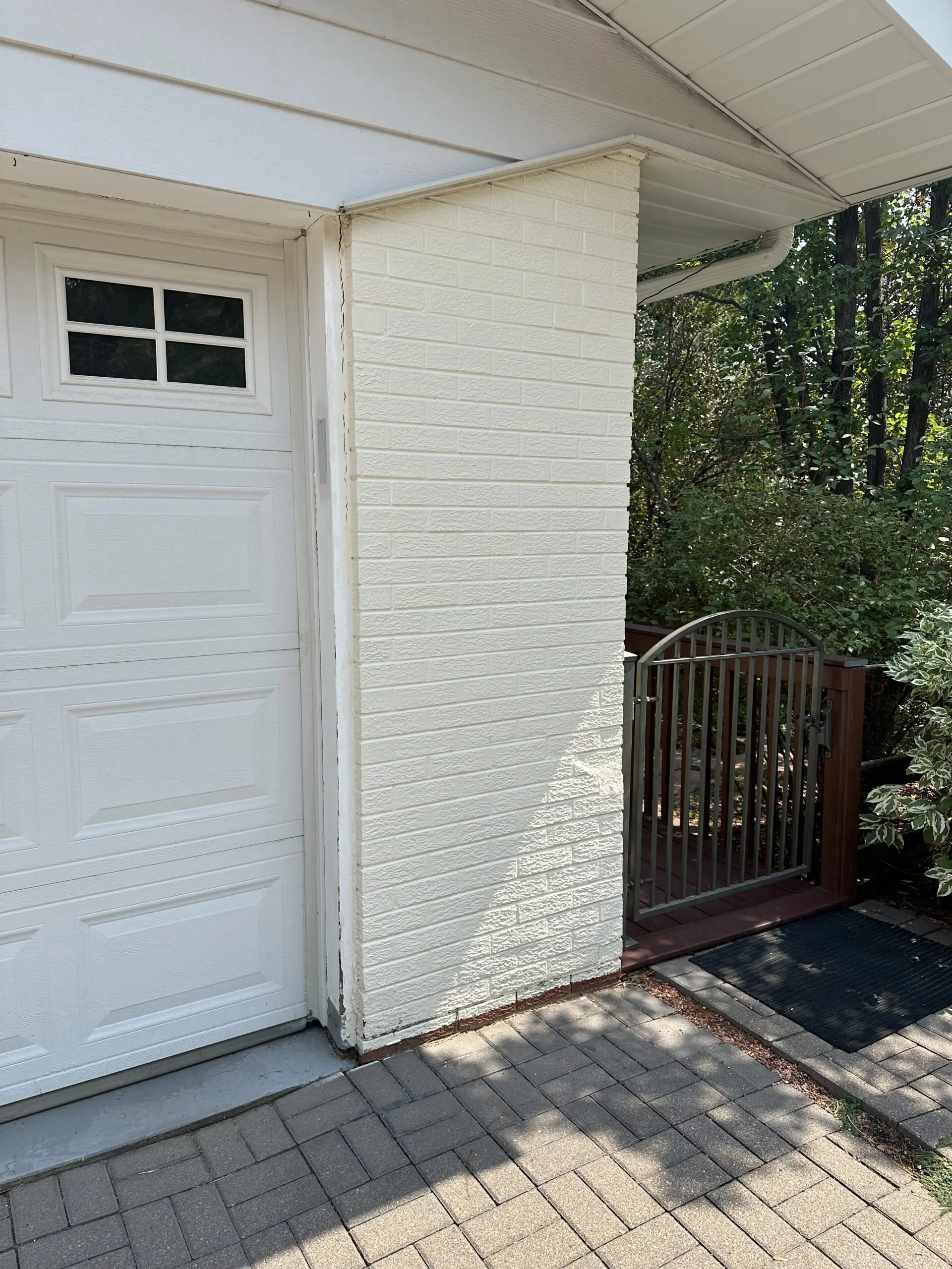 A newly painted white brick exterior outside with a gate, porch and trees to the right.