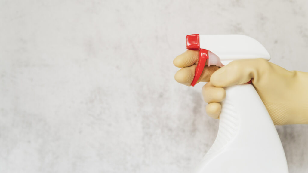 A person holding a spray bottle with a gloved hand.