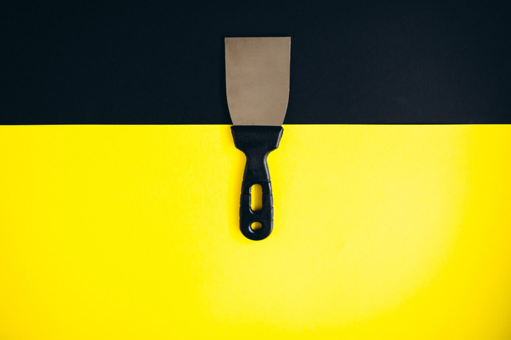 Putty knife on a black and yellow background that can be used for scraping for interior design work.
