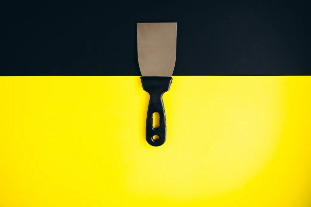 Putty knife on a black and yellow background that can be used for scraping for interior design work.